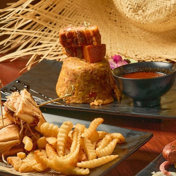 Dominican mofongo with pork belly, a sandwich, crinkle-cut fries, and a bowl of sauce.