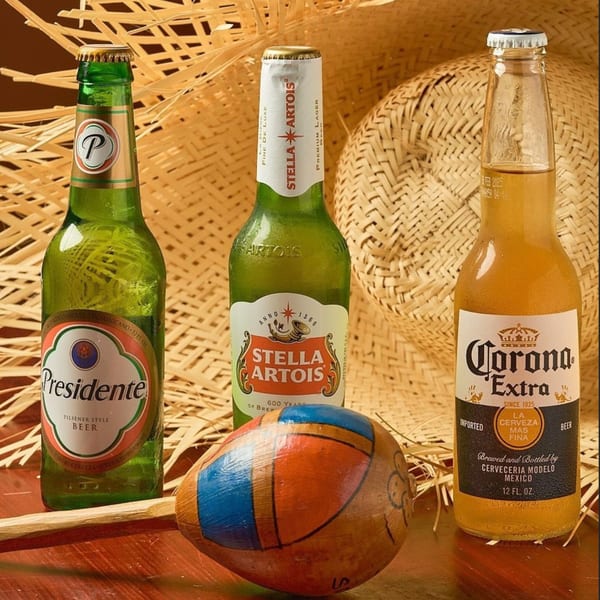 Three beer bottles, Presidente, Stella Artois, and Corona, with a painted coconut and straw hat.