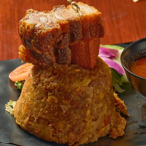 Mofongo topped with crispy fried pork belly, served with a side of sauce and salad.