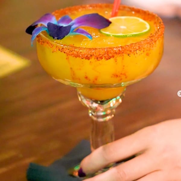 A vibrant yellow frozen drink, garnished with a lime slice and purple orchid, on a wooden table.