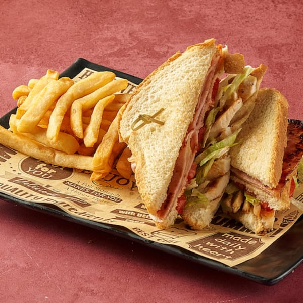Club sandwich with ham, chicken, lettuce, and tomato, served with golden french fries.