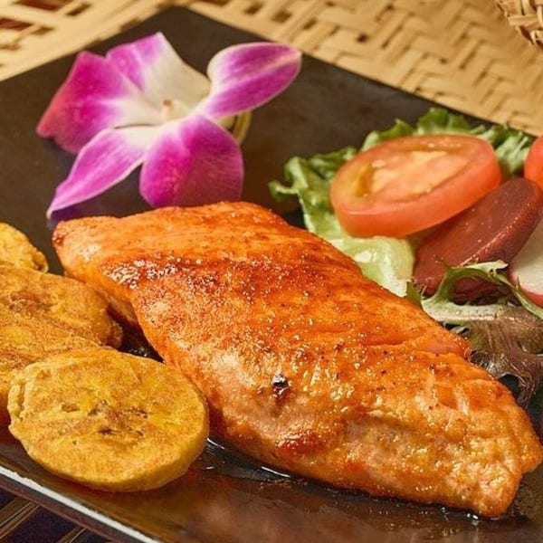 Dominican fried fish with tostones, salad, and a purple orchid garnish on a black plate.